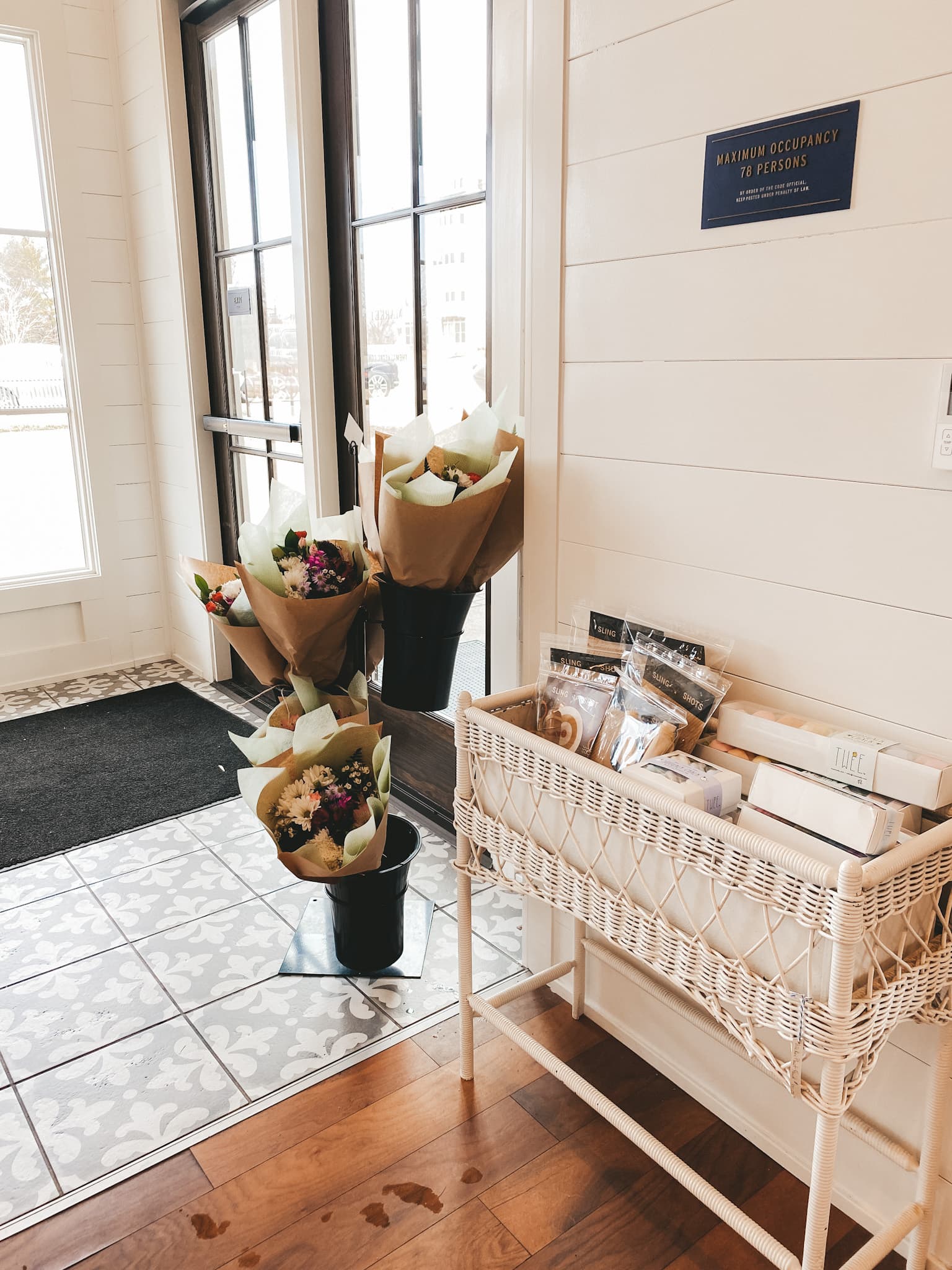 a picture of a coffee shop with a flower stand and a white woven table with products for sale