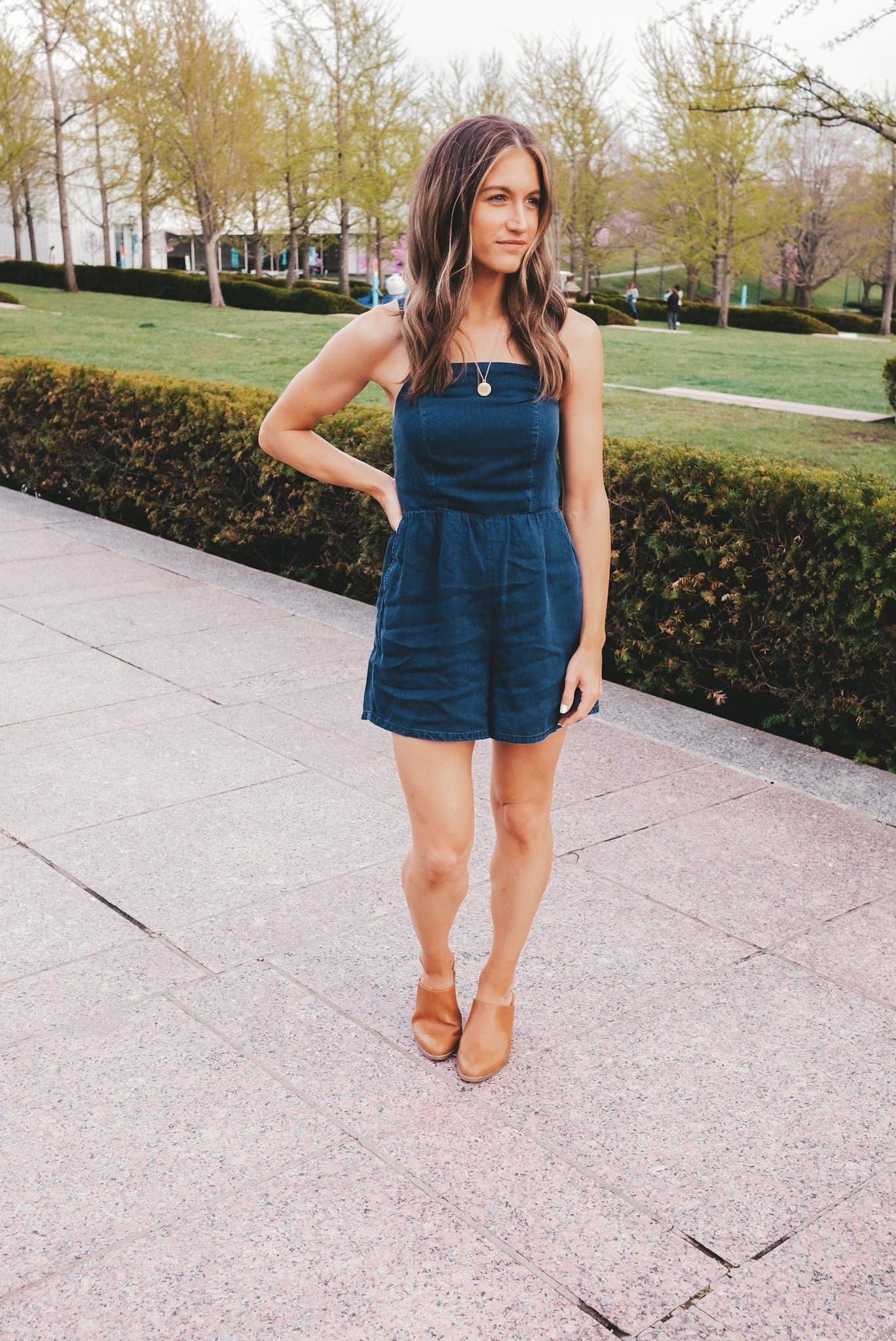 ashley wearing a chambray romper and heeled mules standing next to a hedge at The Nelson-Atkins Museum in Kansas City