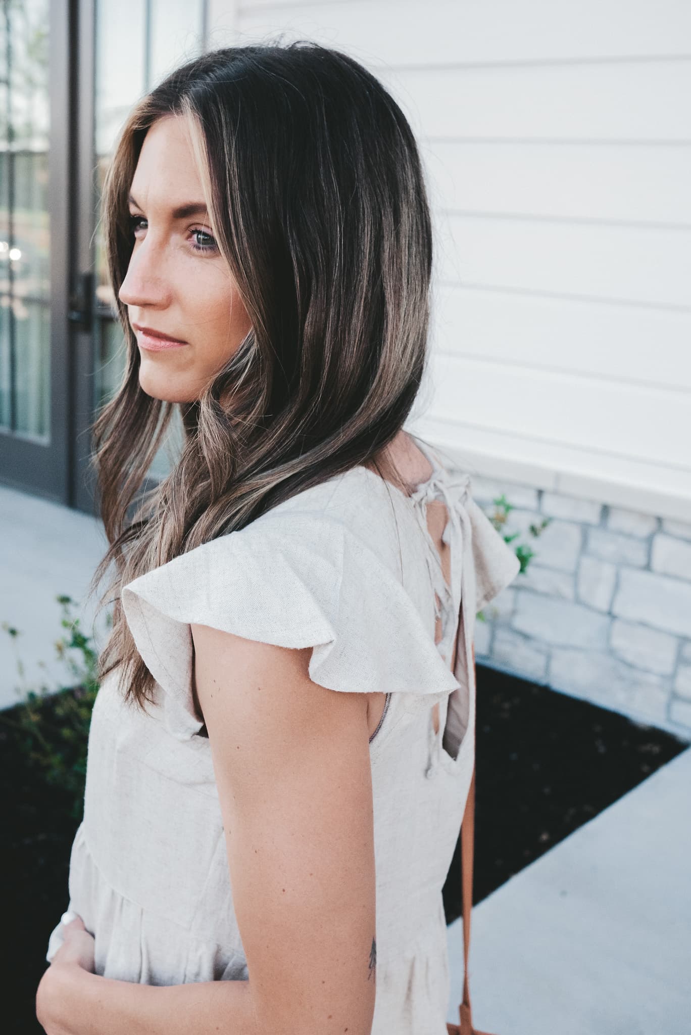 ashley wearing a beige linen flutter sleeve top standing next to a white building