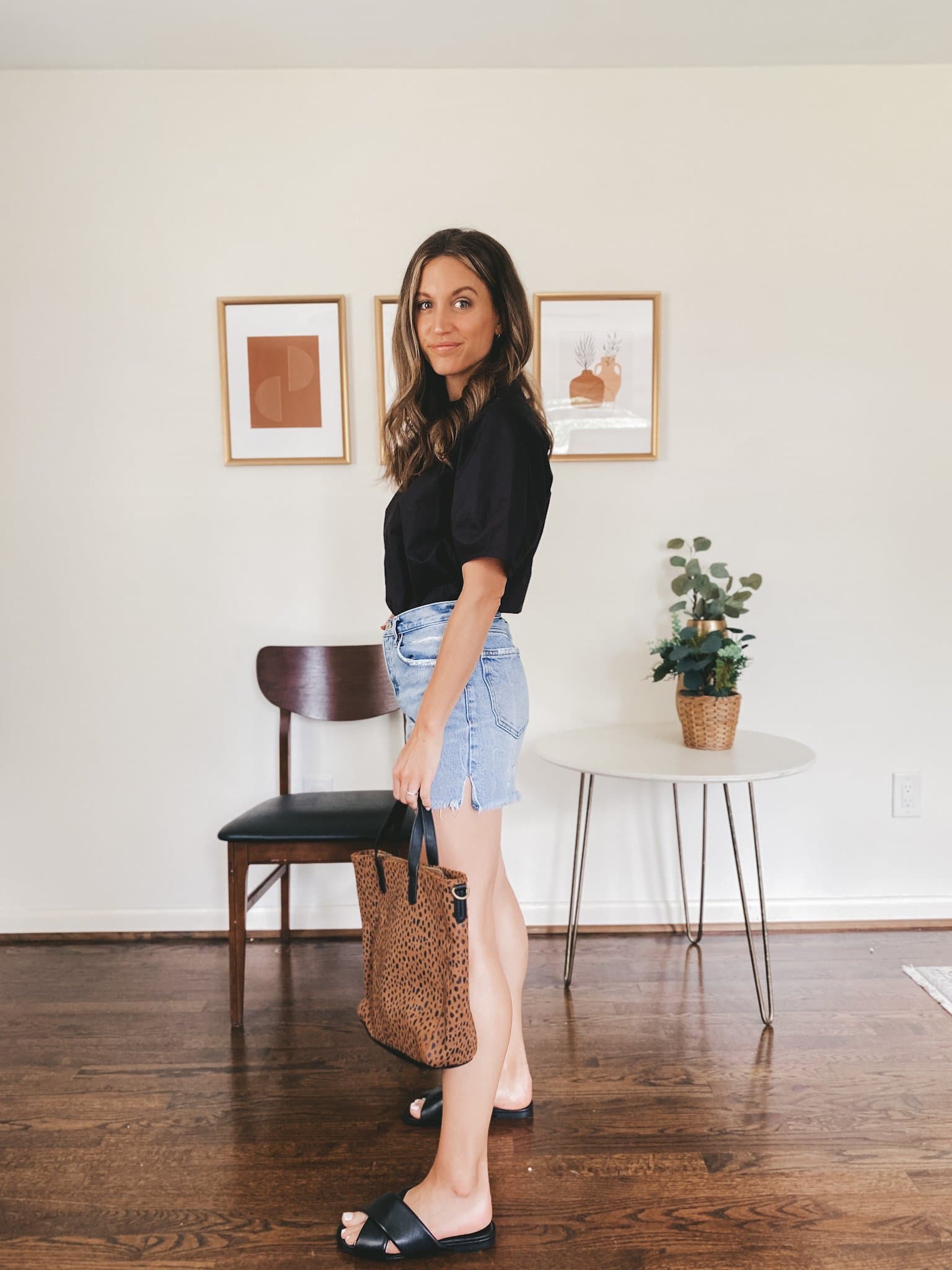 ashley wearing a black top with denim cut-off shorts, black crossover slides and a leopard print tote bag