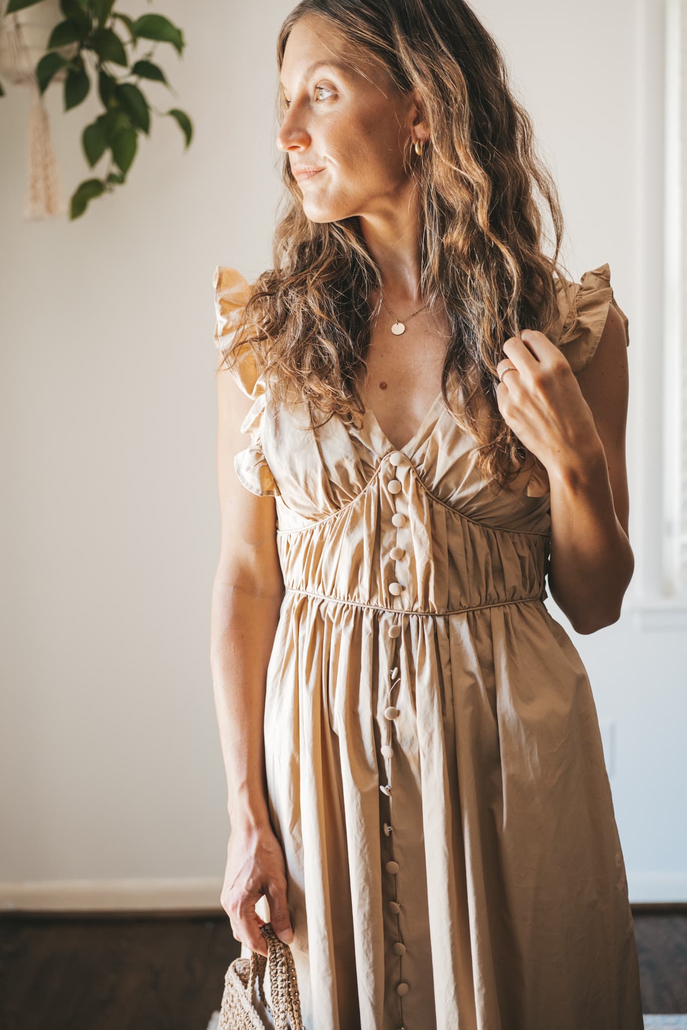 ashley wearing a tan midi dress with fabric buttons, nude sandals, and a woven bag
