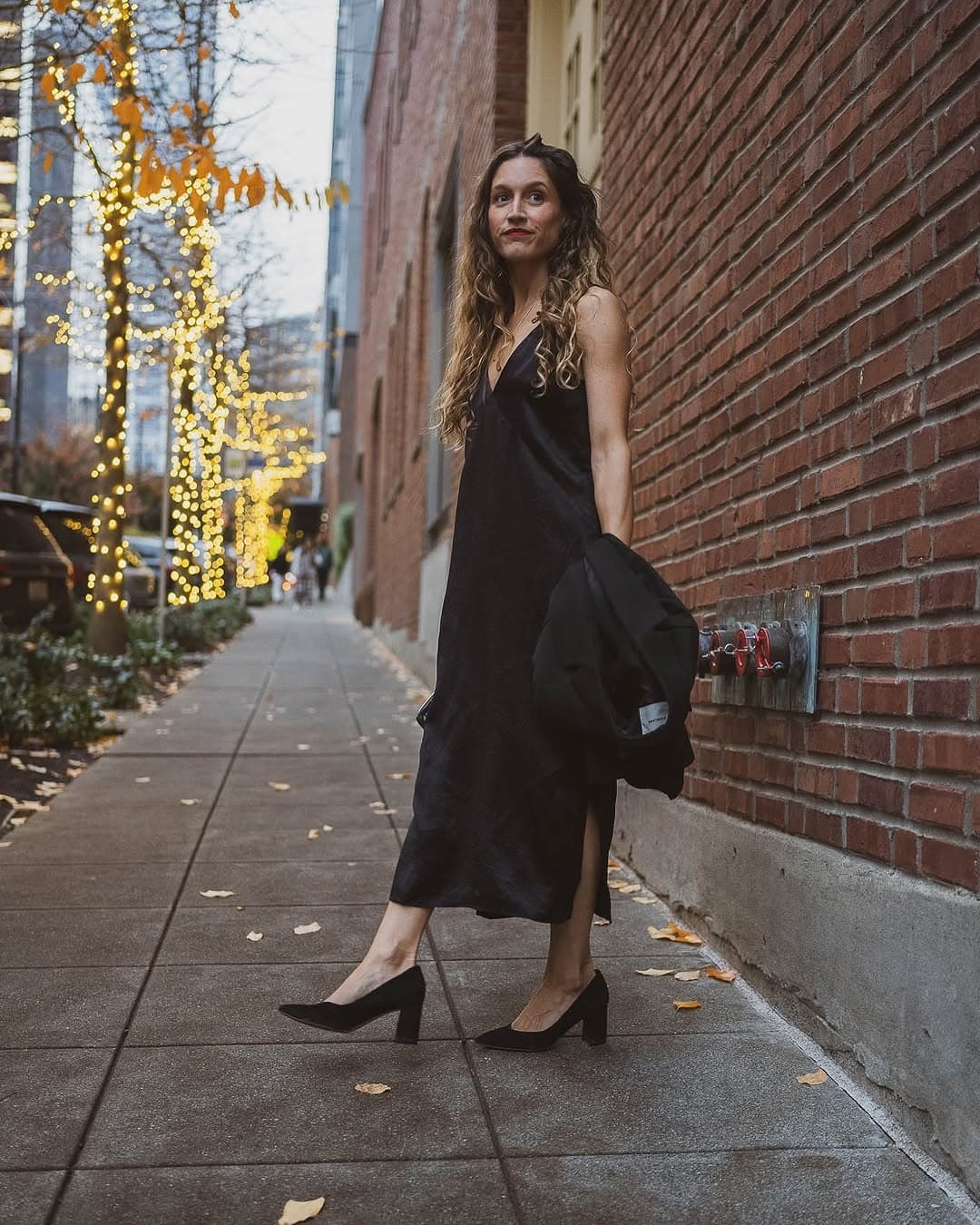 Black satin slip dress with heels, holiday lights in background
