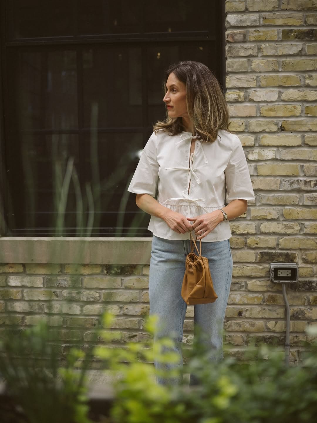 White tie-front top with light wash jeans against a brick wall
