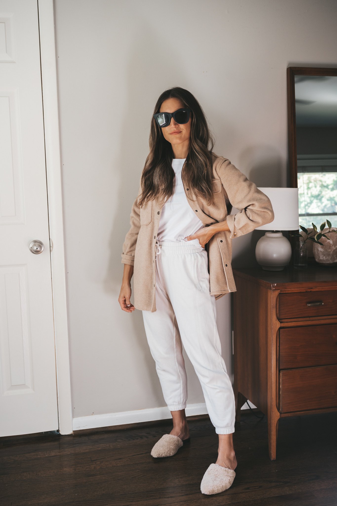 ashley wearing a white tee, tan shacket, white joggers, shearling mules and black square frame sunglasses