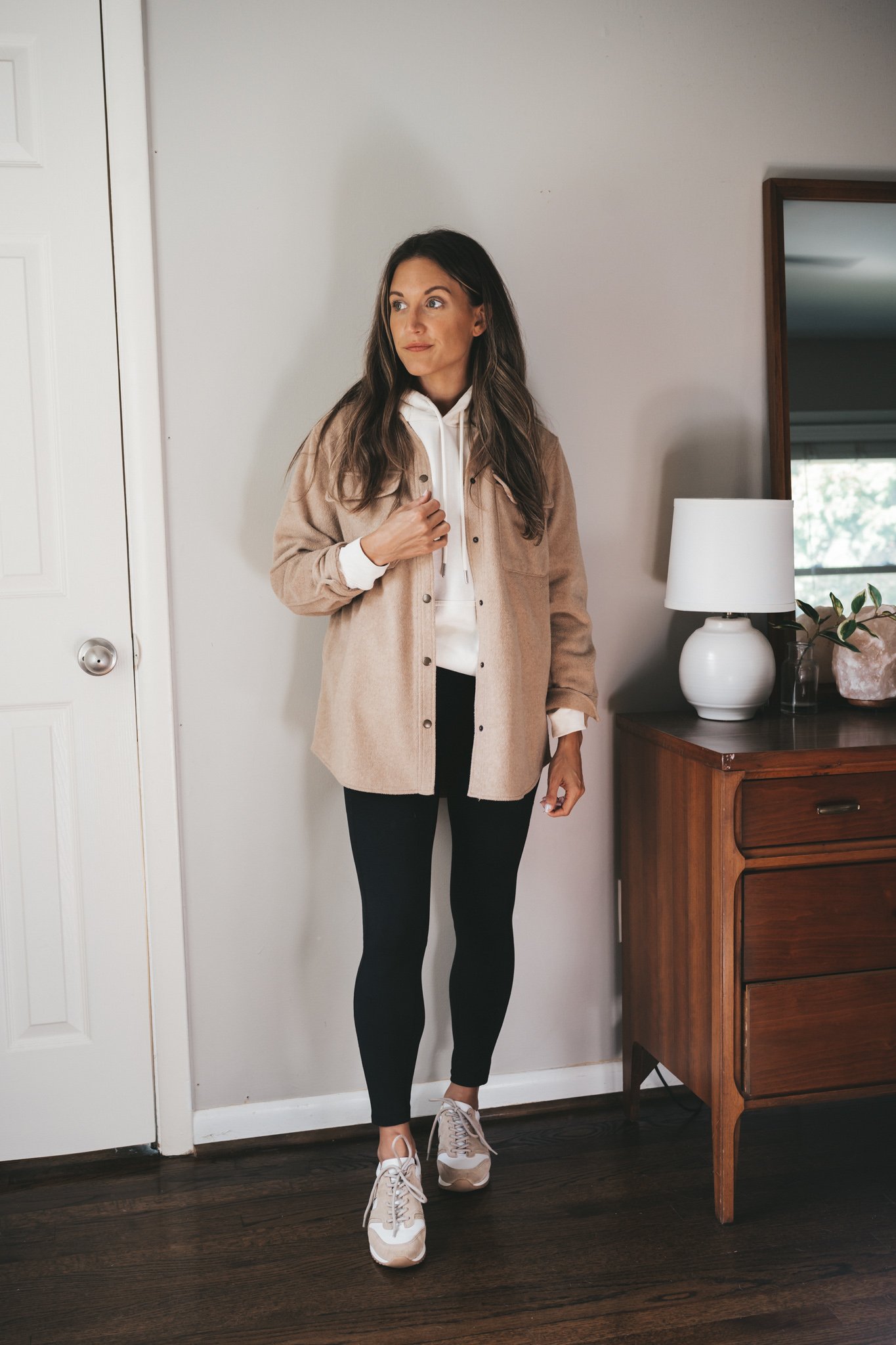ashley wearing a cream colored hoodie, tan shacket, black leggings, and white and tan leather sneakers