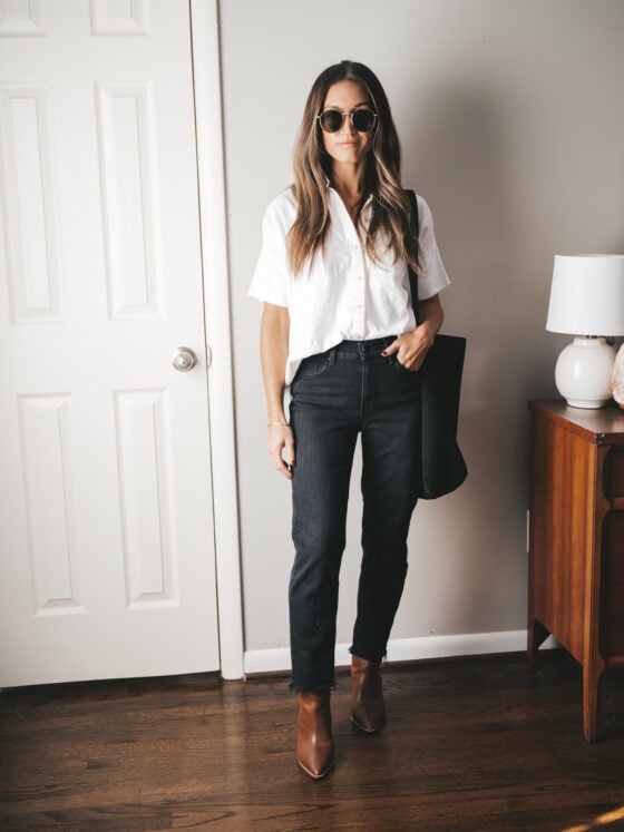 ashley wearing a boxy white button down, black mom jeans, brown heeled booties, a black tote bag, and gold frame round sunglasses