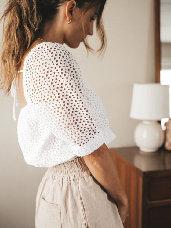 ashley wearing a white puff sleeve eyelet top, tan linen blend shorts, nude sandals, and a gray shoulder bag