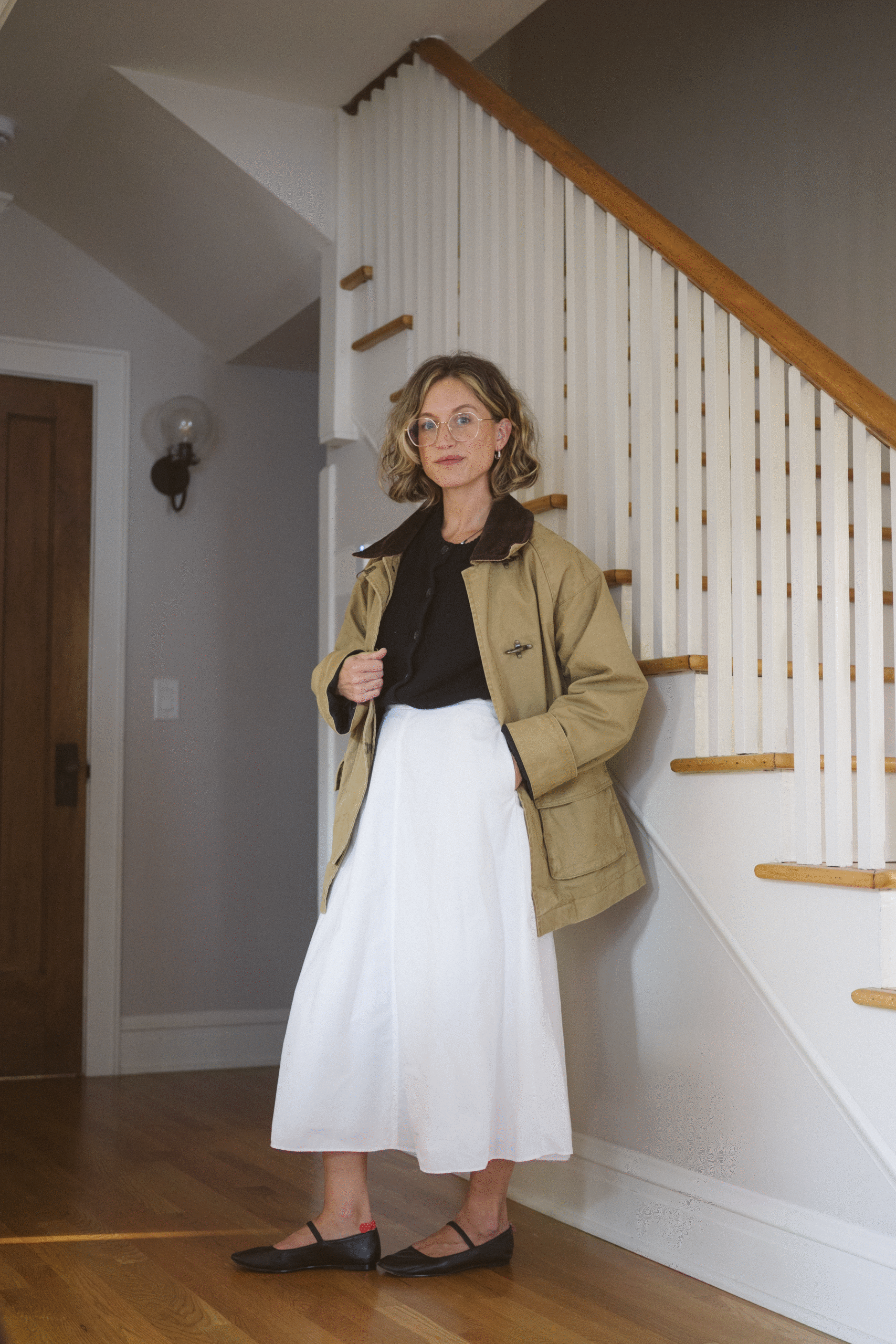 fall outfit with a black cardigan, white poplin skirt, barn jacket, and black mary janes.