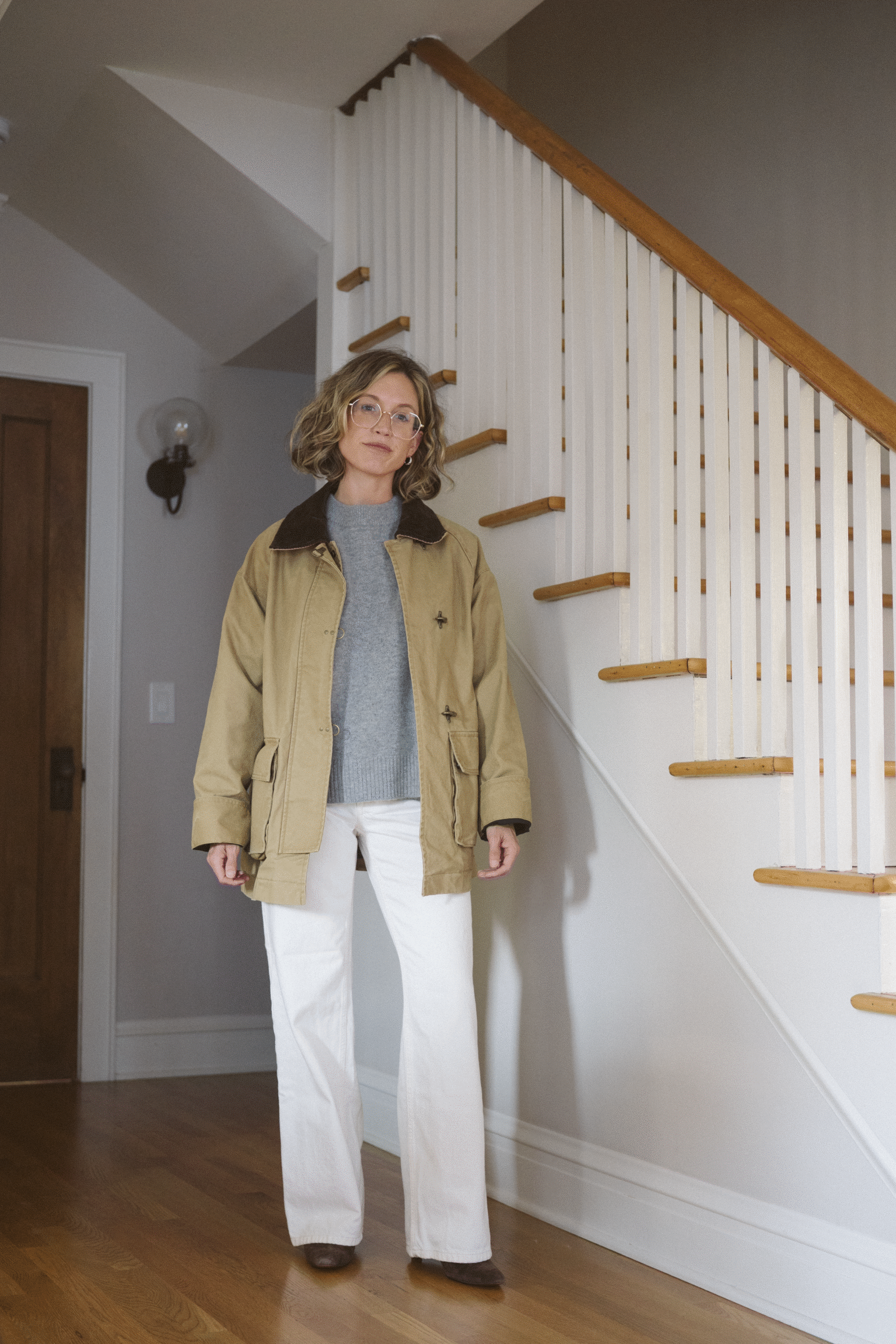 fall outfit with a barn jacket, gray cashmere sweater, white full length jeans, and brown ankle boots