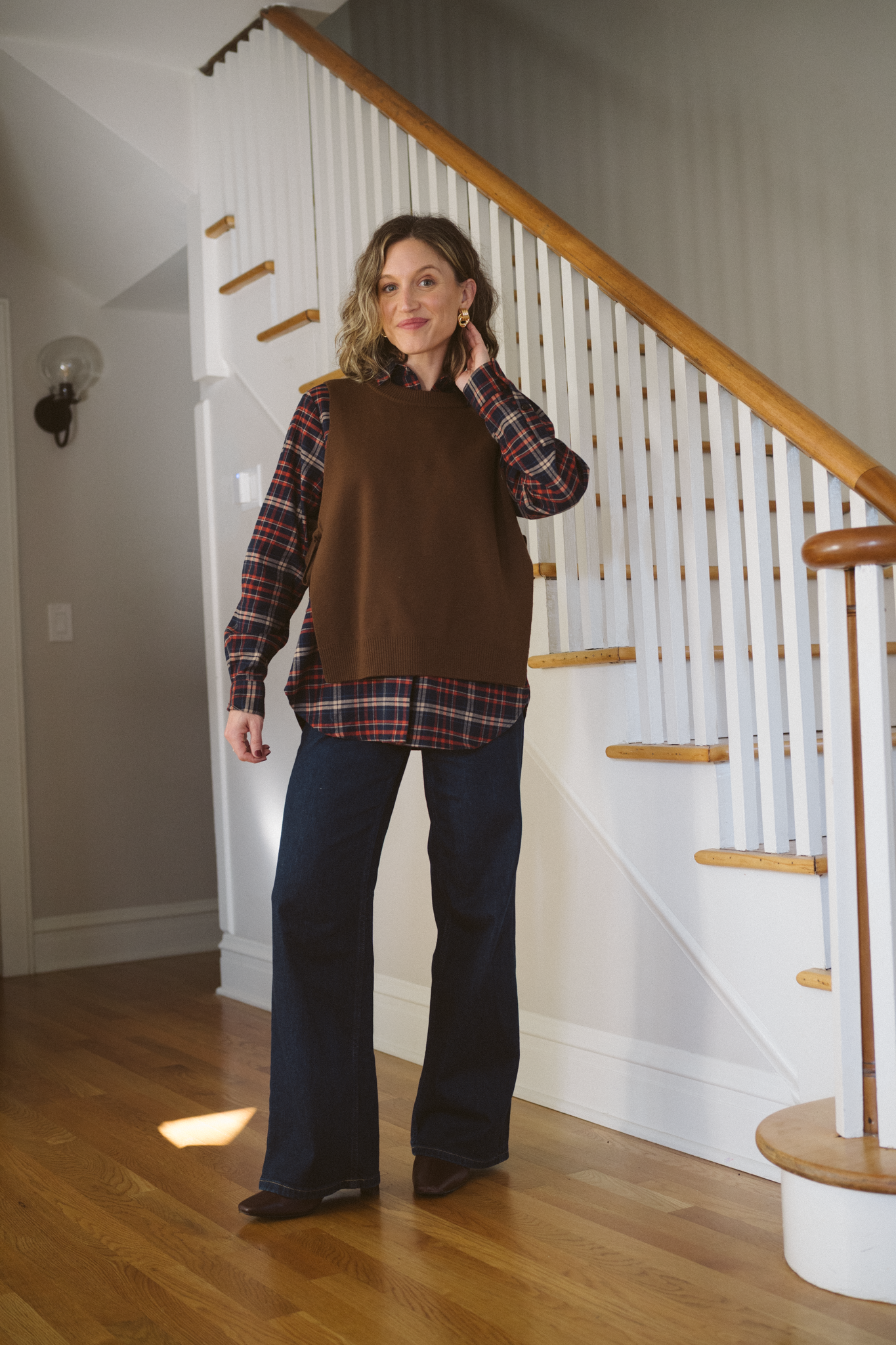 thanksgiving outfit for 2025 with a plaid shirt under a brown sweater vest, dark wash jeans, and brown heeled ankle boots