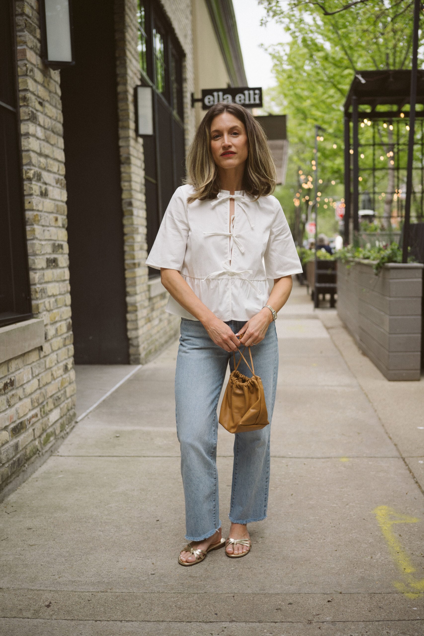 Quince rigid denim review - ashley wearing a white blouse with ties in the front, Quince rigid denim in a light wash, and gold sandals
