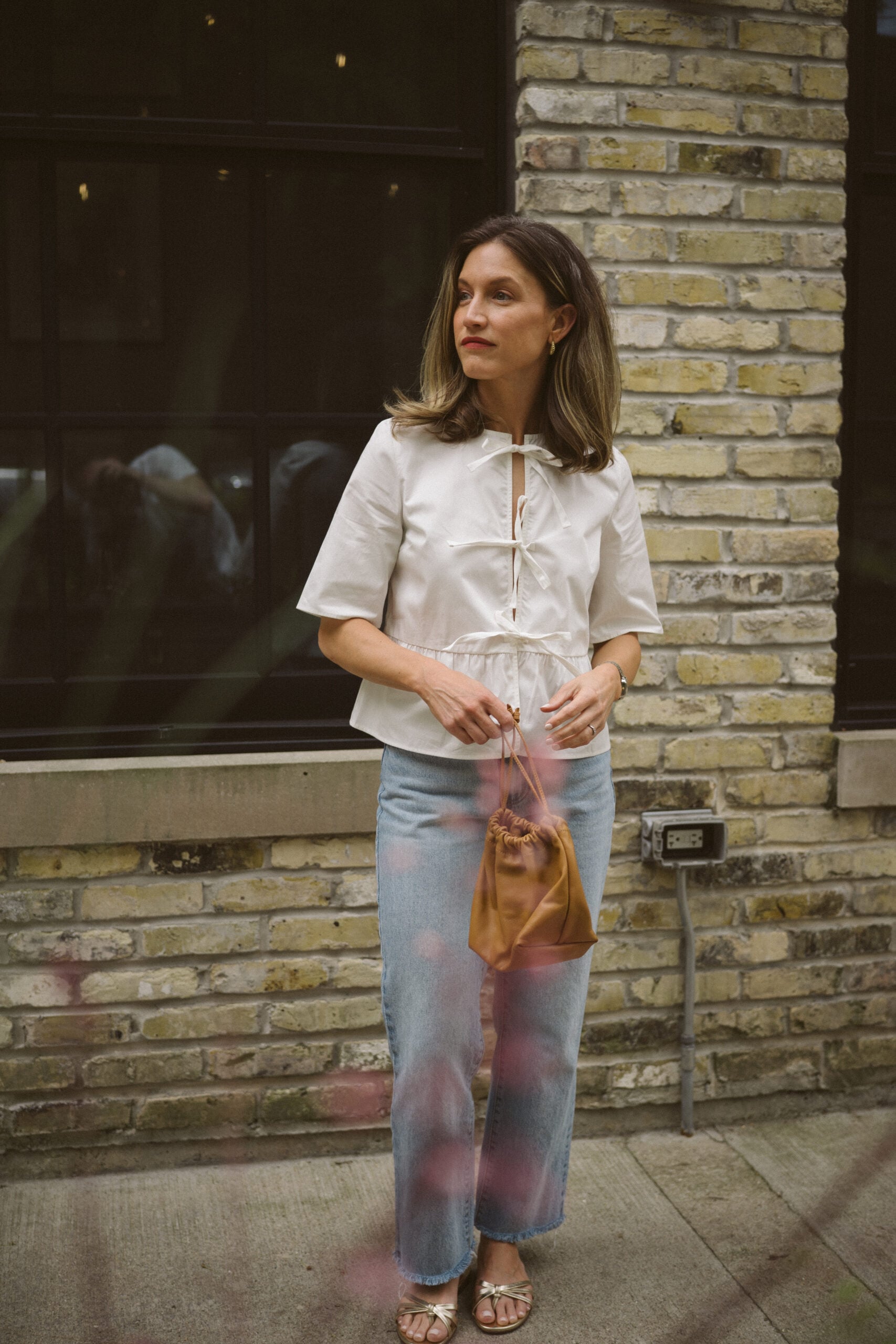 Quince rigid denim review - ashley wearing a white blouse with ties in the front, Quince rigid denim in a light wash, and gold sandals