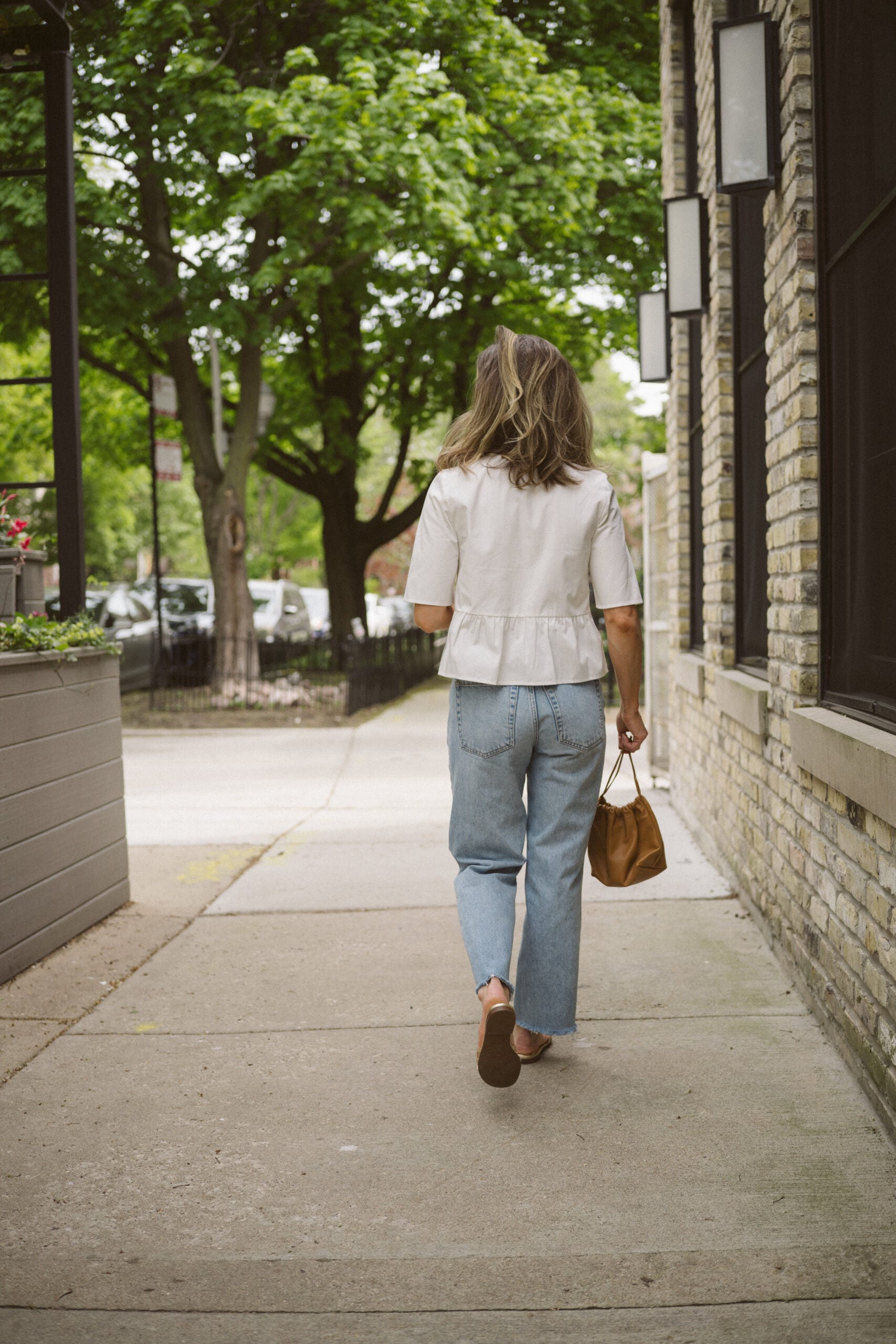 Quince rigid denim review - ashley wearing a white blouse with ties in the front, Quince rigid denim in a light wash, and gold sandals