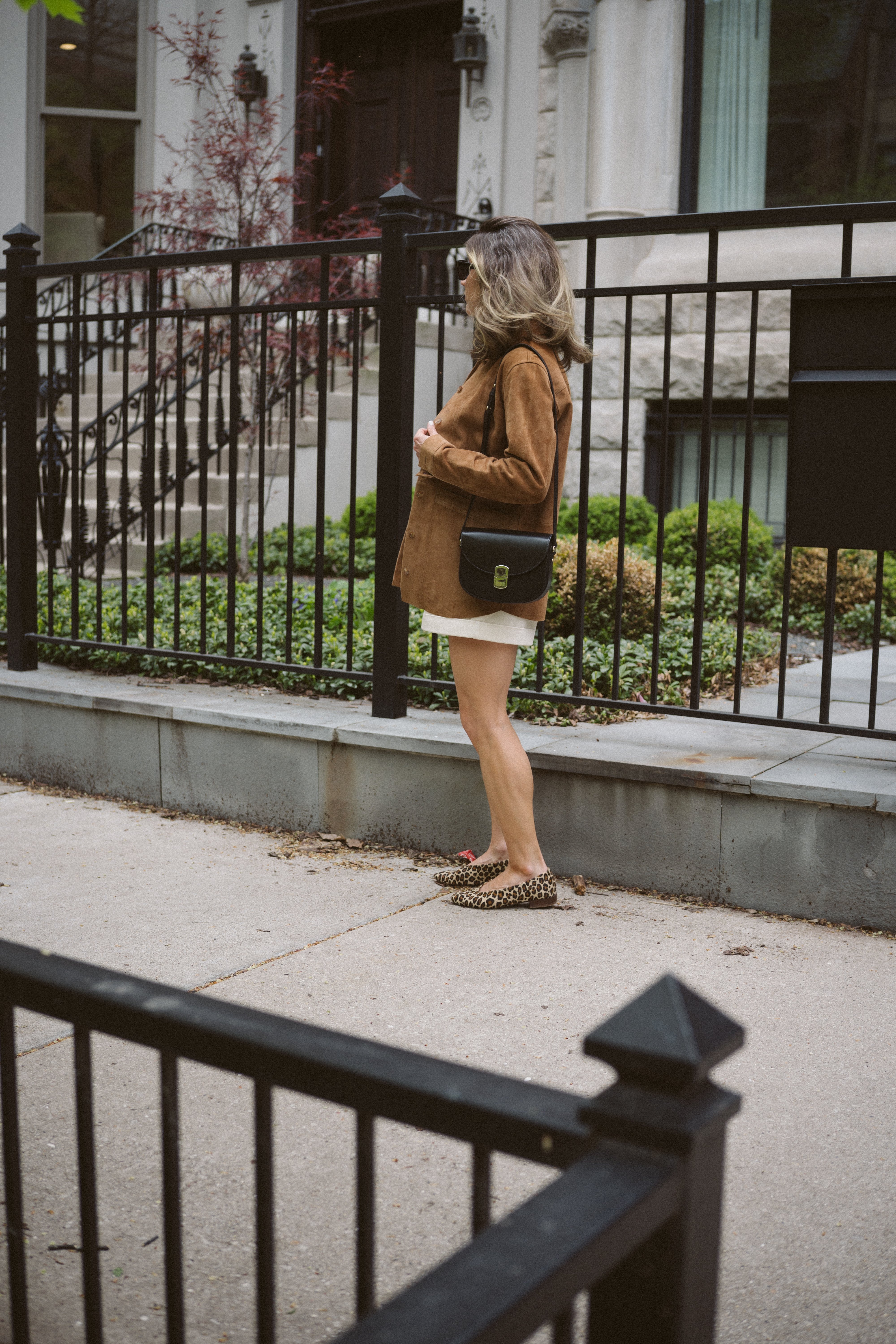 ashley wearing a suede leather jacket, white shorts, and leopard print ballet flats on a city street 