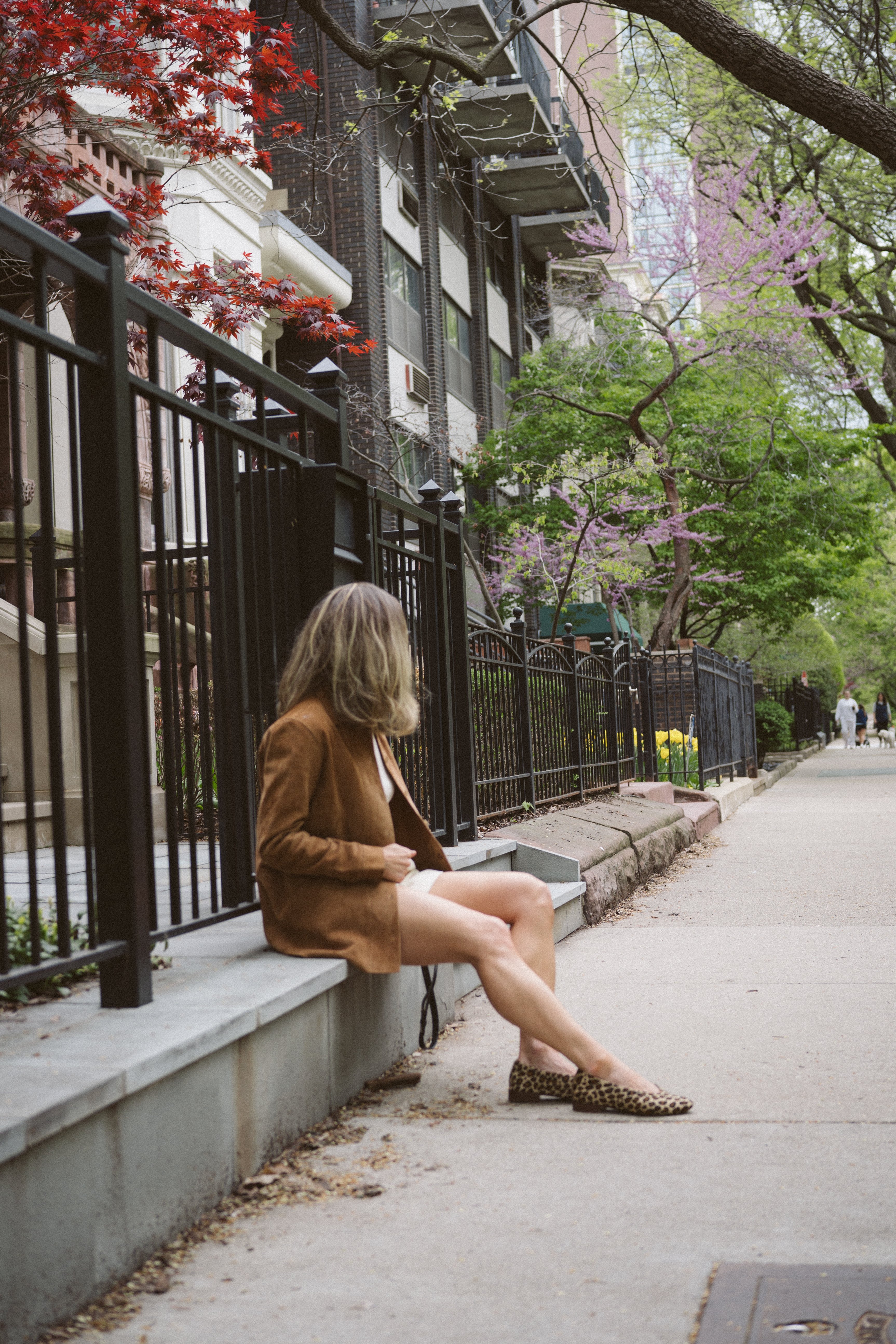 ashley wearing a suede leather jacket, white shorts, and leopard print ballet flats on a city street 